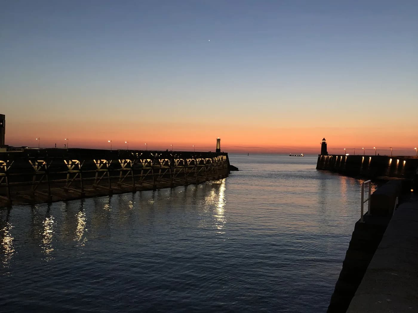 Photo d'origine : les deux jetées d'un port et son phare au coucher du soleil