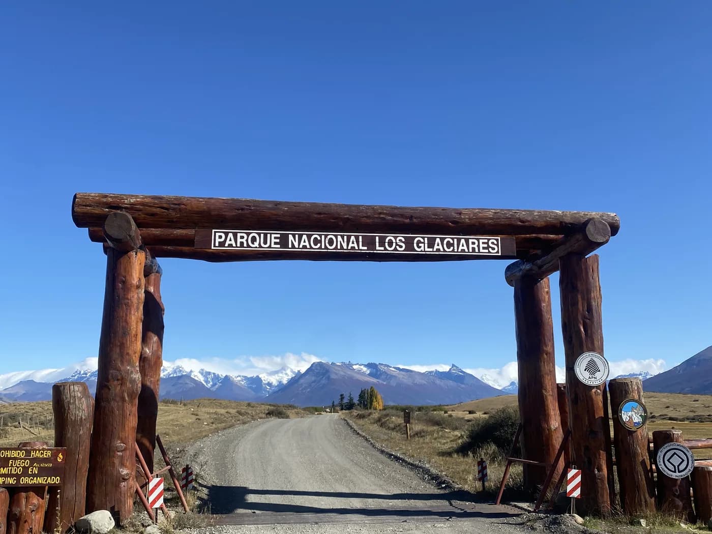 Photo d'origine : le portique en rondins du parc national, la piste et les sommets enneigés au fond